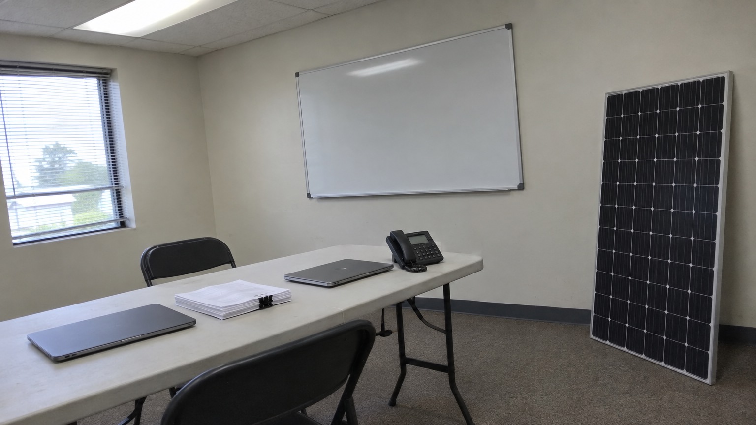 A small solar company office with a folding table, a desk phone and a sample solar panel against the wall