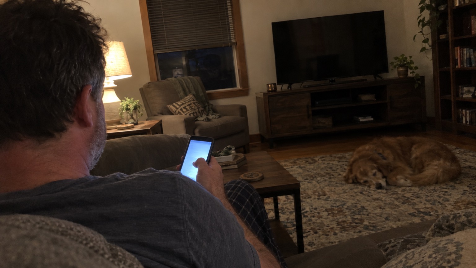 A man on his couch in the evening scrolling on his phone
