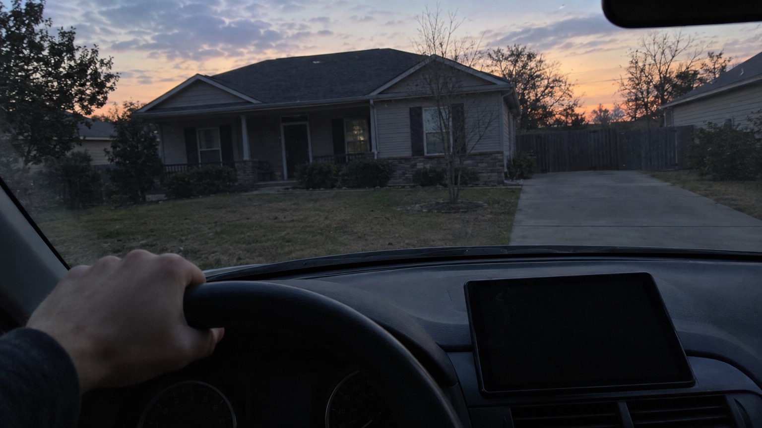 View from a parked car at dusk of a dark house with an empty driveway