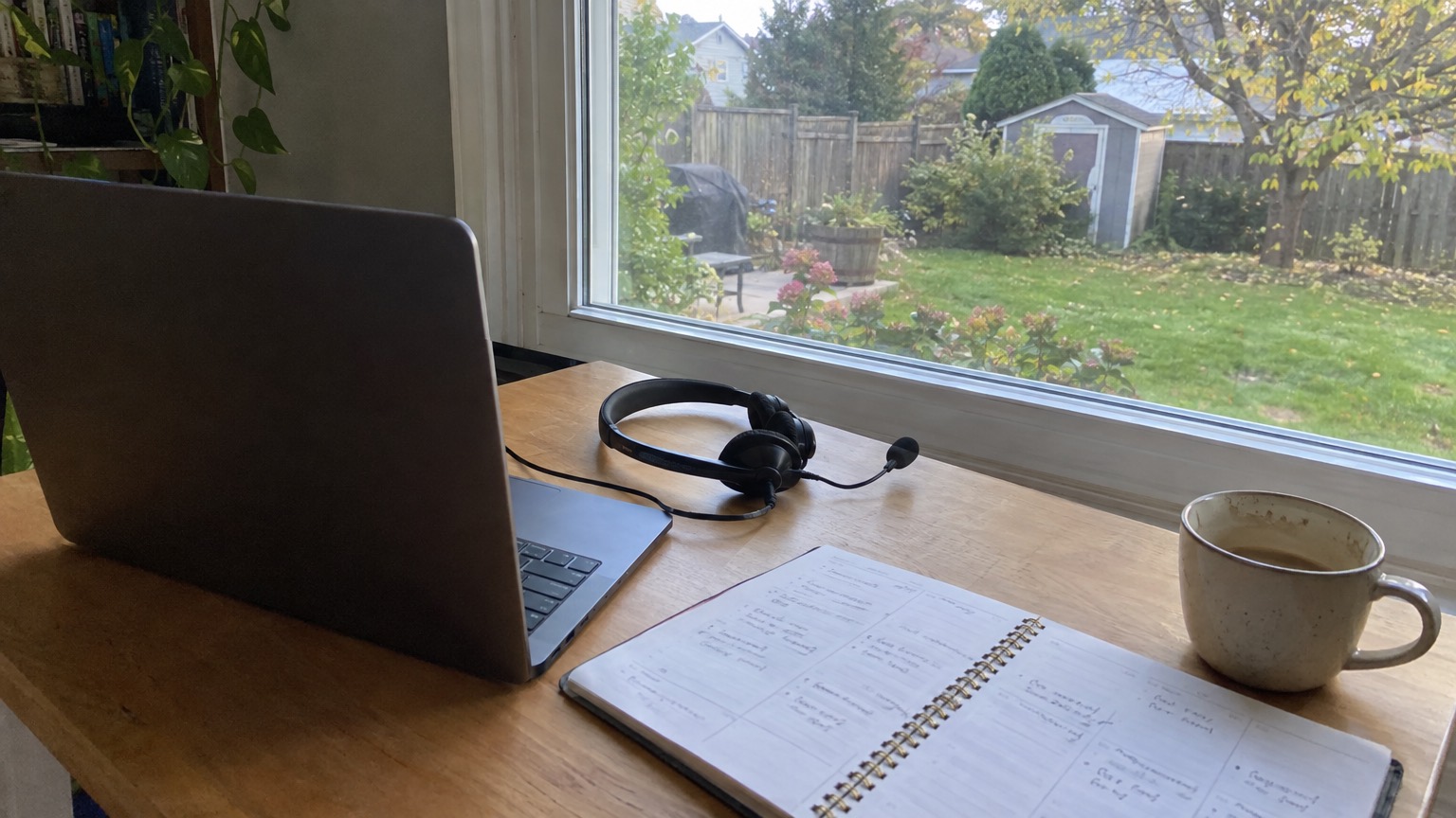 A phone headset, a laptop and an open planner on a home office desk